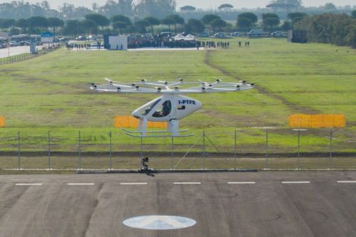 Volocopter 2X wykonuje podejście do lądowania w vertiporcie Rzym-Fiumicino po pierwszym locie załogowym na terenie tego lotniska, wykonanym 6 października br. W oddali widać zgromadzonych obserwatorów / Zdjęcie: Volocopter 