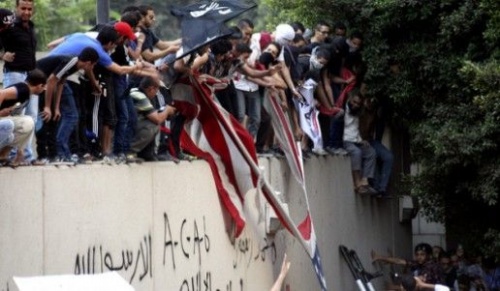Protestujący w Kairze na murze otaczającym ambasadę, drą zerwaną amerykańską flagę / Zdjęcie: Bloomberg